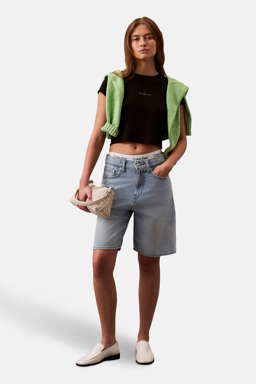 Zwart T-shirt met korte mouwen van Calvin Klein, gedragen met een groene trui die is vastgebonden en een spijkerbroek met korte pijpen.