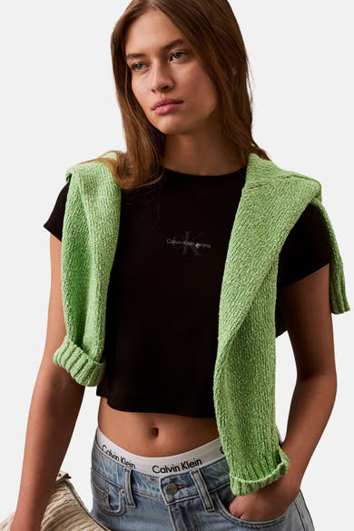 Zwart T-shirt met korte mouwen van Calvin Klein, gedragen met een groene trui geknoopt over de schouders en een low-rise spijkerbroek.