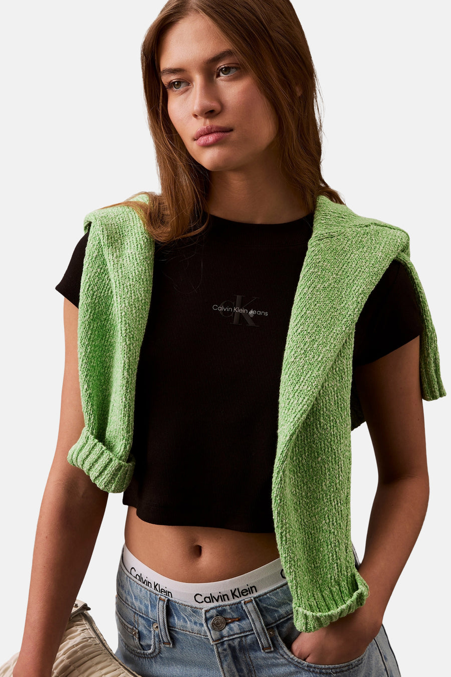 Zwart T-shirt met korte mouwen van Calvin Klein, gedragen met een groene trui geknoopt over de schouders en een low-rise spijkerbroek.