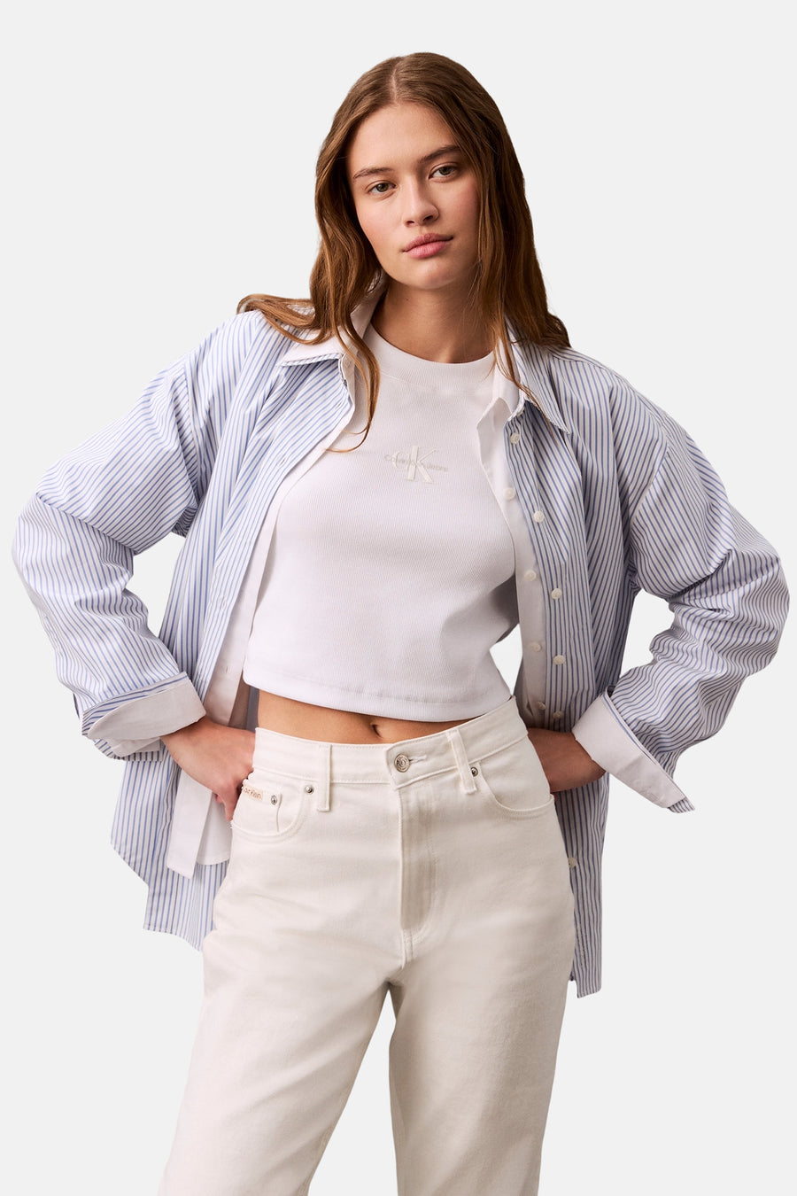 Wit T-shirt met korte mouwen van Calvin Klein, gedragen met een blauw gestreept overhemd en een ecru high-waisted jeans.