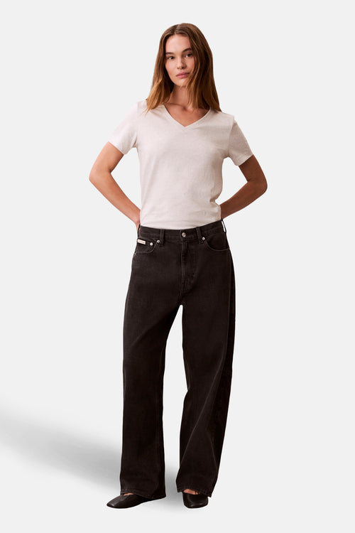 T-shirt à manches courtes beige de Calvin Klein, porté avec un jean noir ample et des chaussures plates.