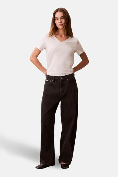 Beige T-shirt met korte mouwen van Calvin Klein, gedragen met een wijde zwarte jeans en platte schoenen.
