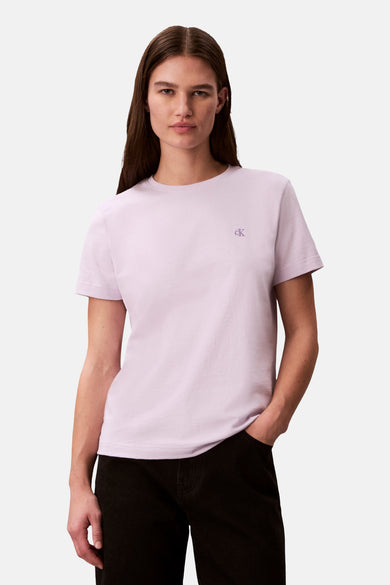 T-shirt à manches courtes mauve de Calvin Klein, avec un logo brodé sur la poitrine et porté avec un jean noir.
