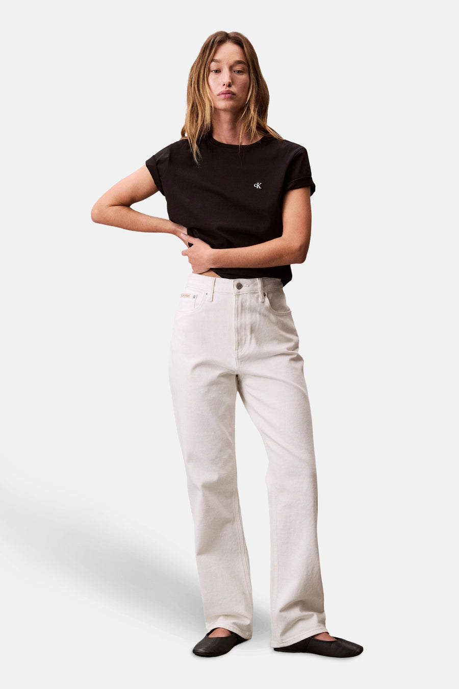 Zwart T-shirt met korte mouwen van Calvin Klein, gedragen met een witte high-waist jeans en zwarte platte schoenen.