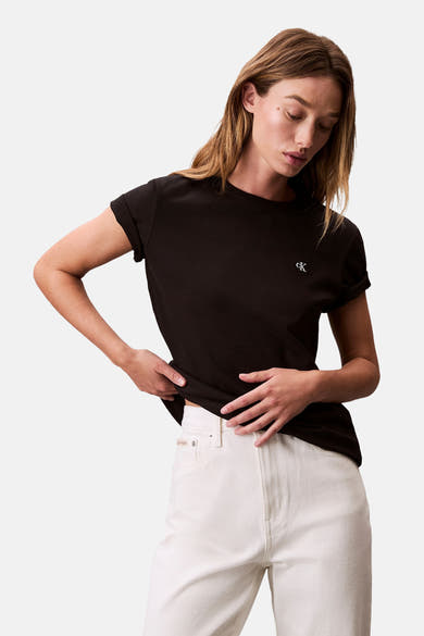 Zwart T-shirt met korte mouwen van Calvin Klein, gedragen met een witte high-waisted jeans, de blik naar beneden gericht.