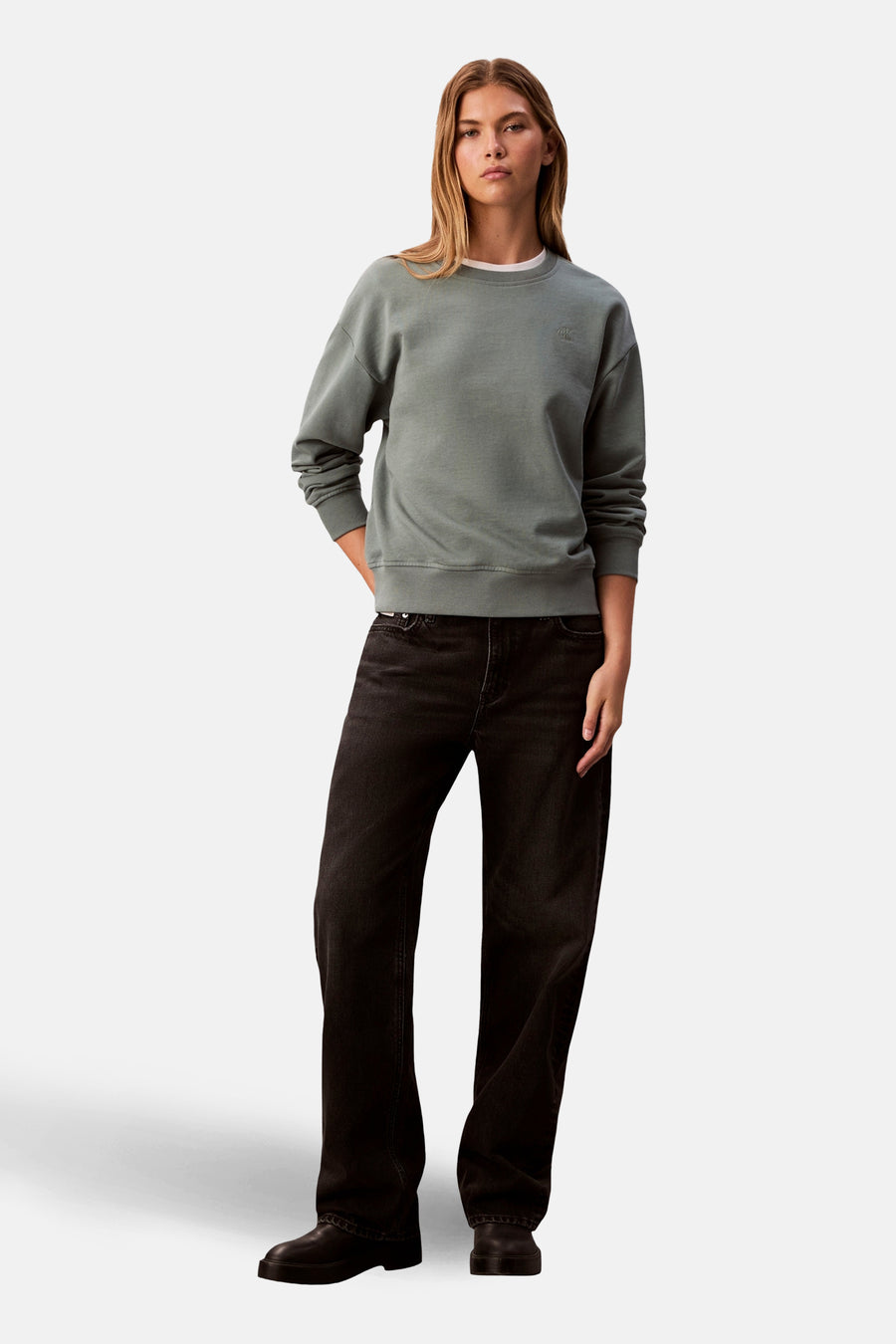Sweat vert col rond de Calvin Klein, porté avec un jean noir ample et des chaussures assorties.