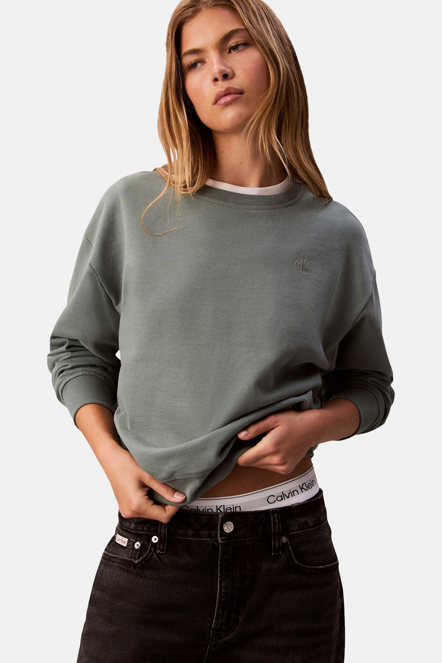 Sweat-shirt vert de Calvin Klein, porté avec un t-shirt blanc et un jean noir taille haute.
