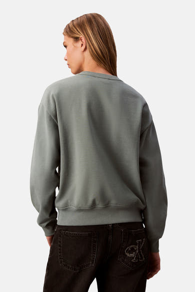 Sweat-shirt vert de Calvin Klein, coupe ample, porté avec un jean noir à logo sur la poche arrière.