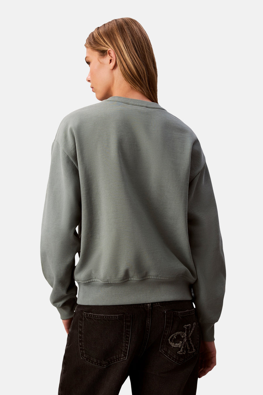 Sweat-shirt vert de Calvin Klein, coupe ample, porté avec un jean noir à logo sur la poche arrière.