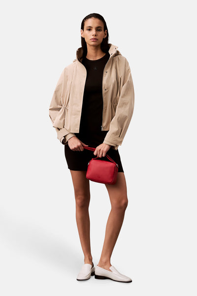 Robe courte noire de Calvin Klein, portée avec une veste beige, un sac rouge et des mocassins blancs.