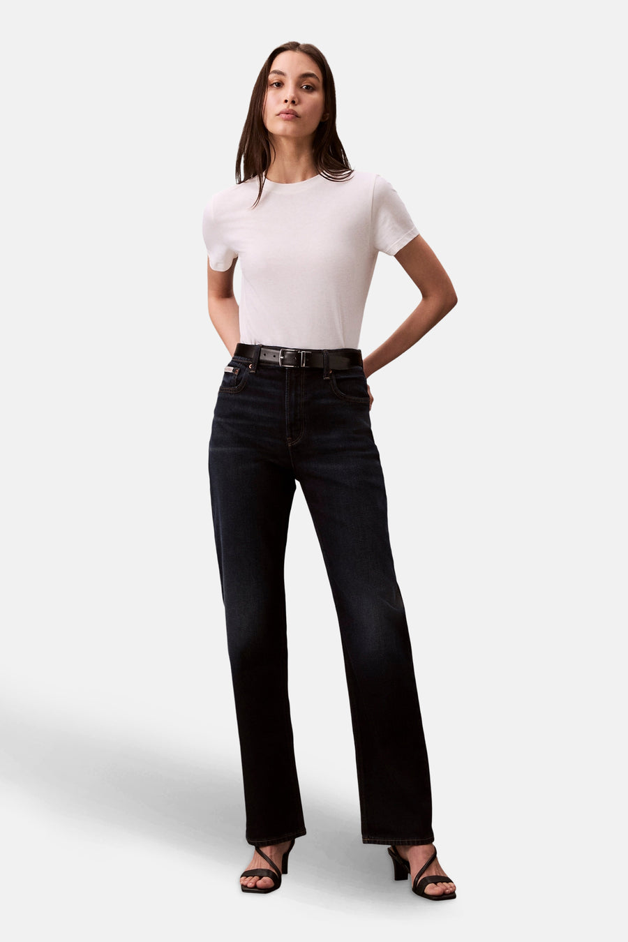 Rechte donkerblauwe spijkerbroek van Calvin Klein, gedragen met een effen wit T-shirt, een zwarte riem en hakken.