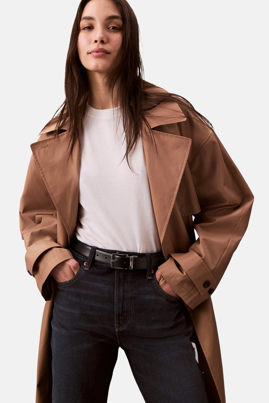 Rechte donkerblauwe spijkerbroek van Calvin Klein, gedragen met een lichtbruine trenchcoat.