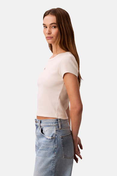 Ecru T-shirt met korte mouwen van Calvin Klein, in fijne ribgebreide stof, gedragen met een high-waisted jeans.