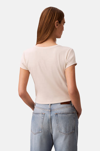 Ecru T-shirt met korte mouwen van Calvin Klein, in ribgebreide stof, gedragen met een high-waisted jeans.