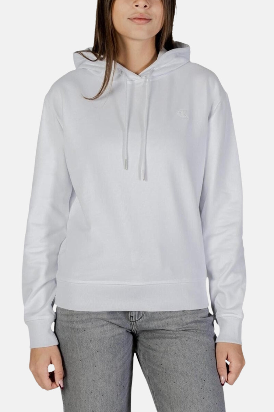 Sweat à capuche blanc de Calvin Klein, avec cordon de serrage et logo discret sur le devant, porté avec un jean gris.
