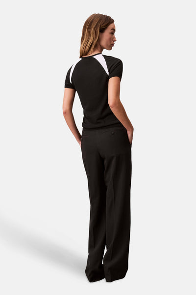 T-shirt noir à manches courtes de Calvin Klein, avec empiècements blancs aux épaules, porté avec un pantalon noir taille haute.
