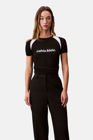 T-shirt noir à manches courtes de Calvin Klein, avec rayures blanches aux épaules, porté avec un pantalon noir.
