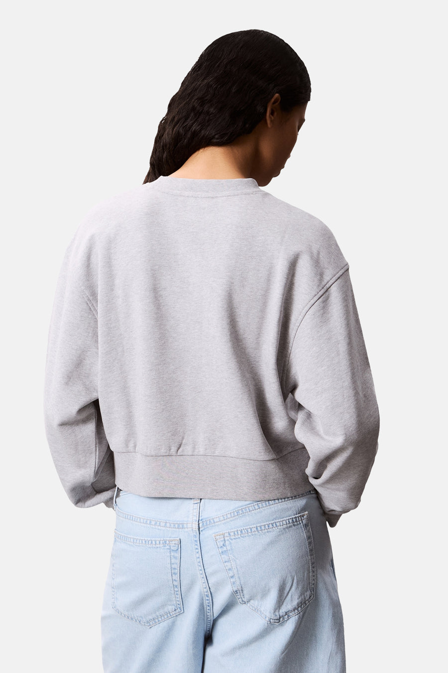 Sweatshirt col rond gris de Calvin Klein, présenté de dos, porté avec un jean bleu clair.
