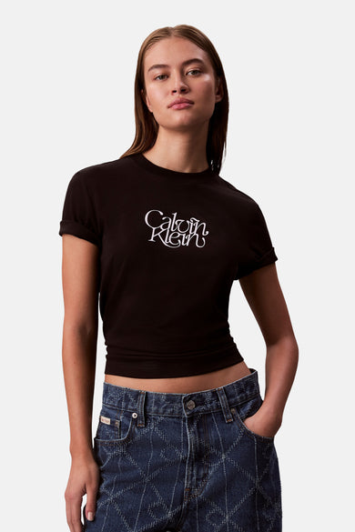 Zwart T-shirt met korte mouwen van Calvin Klein, met een wit logo op de voorkant, gedragen met een blauwe spijkerbroek met patroon.