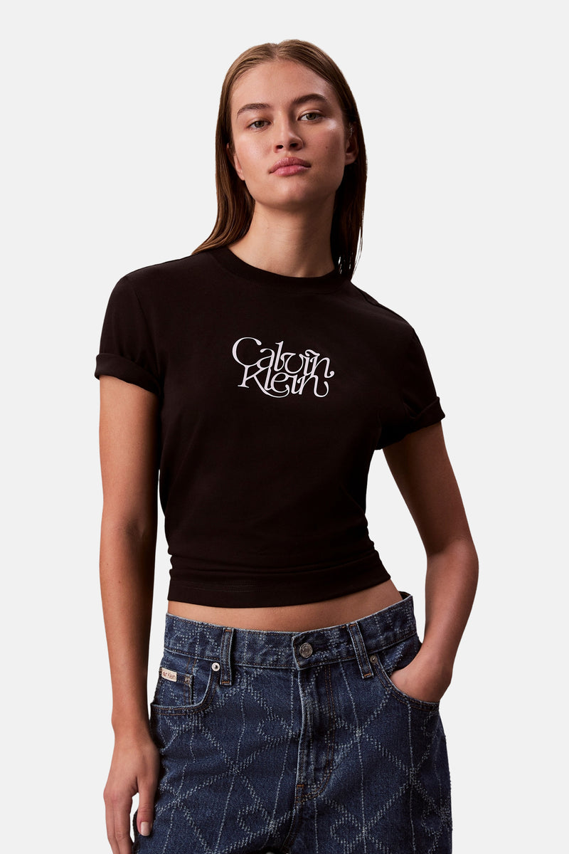 Zwart T-shirt met korte mouwen van Calvin Klein, met een wit logo op de voorkant, gedragen met een blauwe spijkerbroek met patroon.