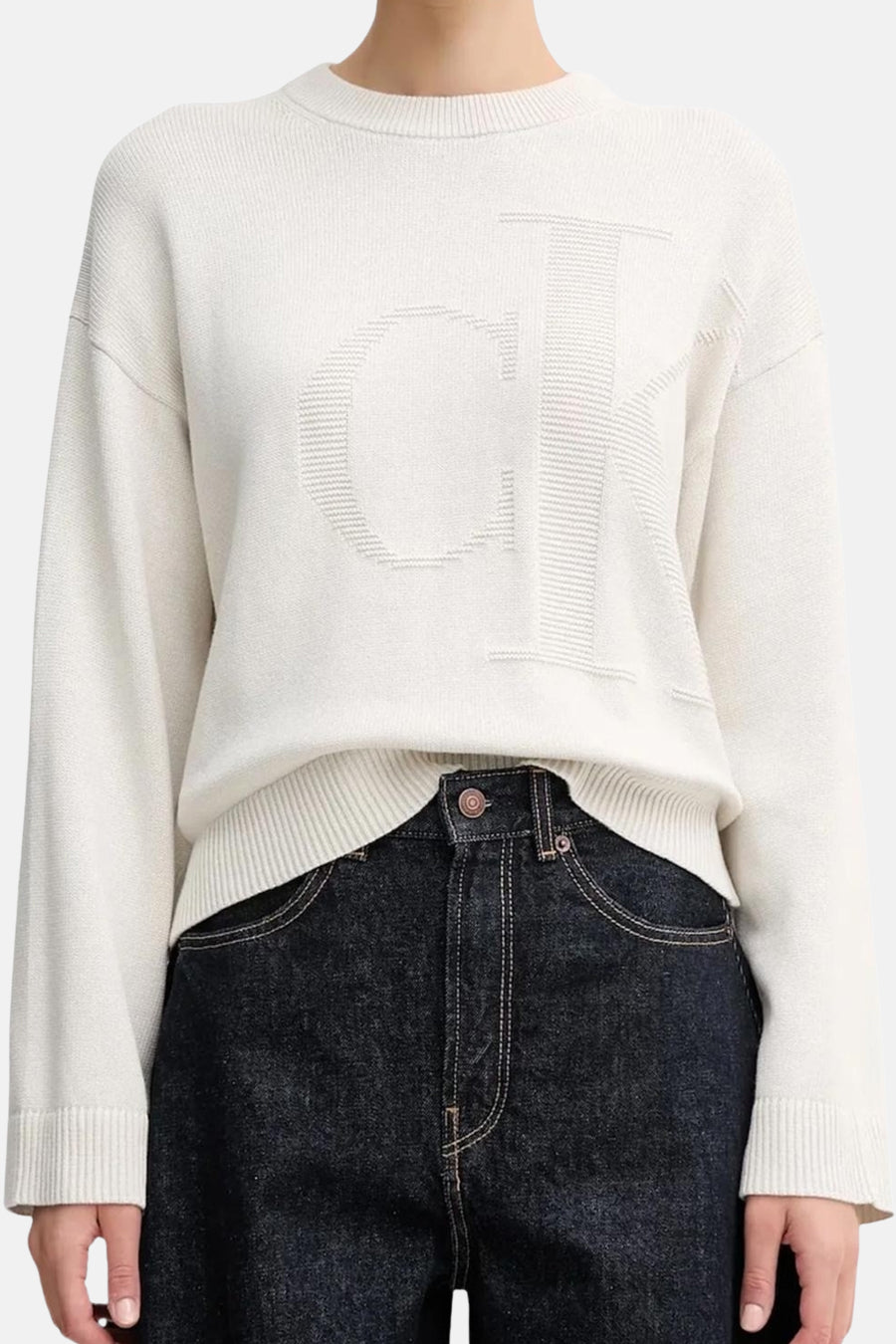 Beige Calvin Klein sweatshirt, met een groot reliëflogo op de voorkant en gedragen met een donkere spijkerbroek.