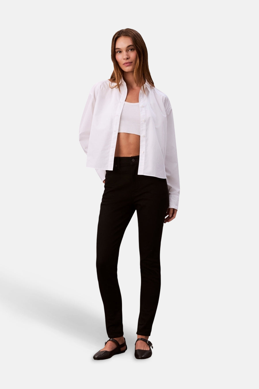 Jean skinny noir taille haute de Calvin Klein, porté avec un top et une chemise blanche.