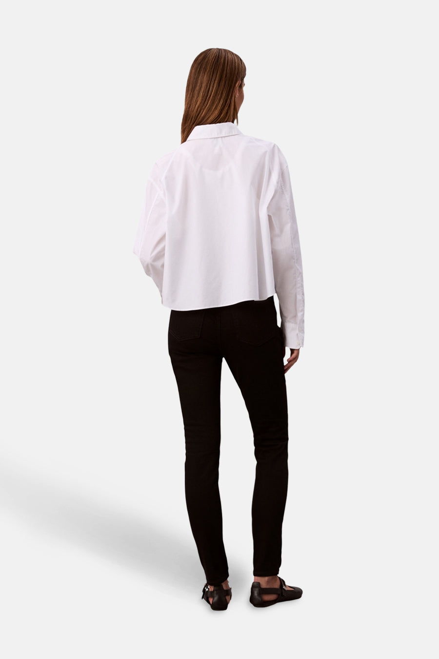 Jeans skinny noirs de Calvin Klein, portés avec une chemise blanche et des chaussures plates noires.