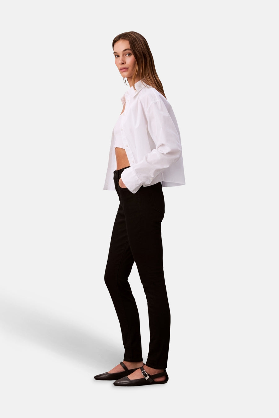 Jean skinny noir de Calvin Klein, porté avec une chemise blanche courte et des chaussures à bride.