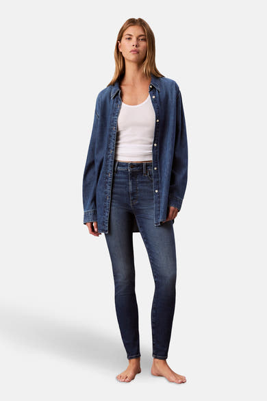 Jean skinny en denim bleu moyen de Calvin Klein, porté avec un débardeur blanc et une chemise en denim.