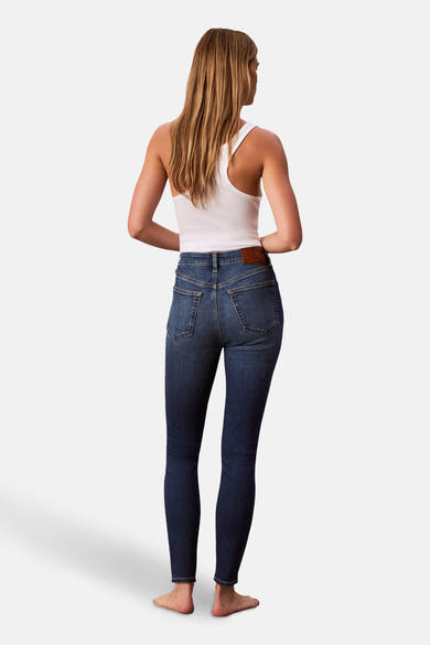 Jean skinny en denim bleu moyen de Calvin Klein, porté avec un débardeur blanc, vue de dos.