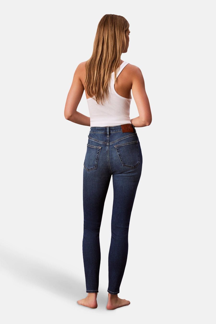 Jean skinny en denim bleu moyen de Calvin Klein, porté avec un débardeur blanc, vue de dos.