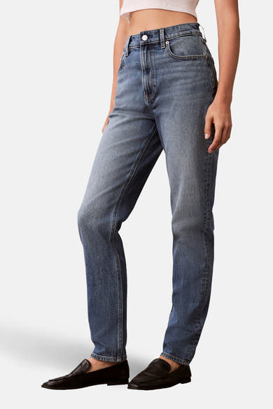 Jean Mom en denim bleu moyen de Calvin Klein, porté avec des mocassins noirs.
