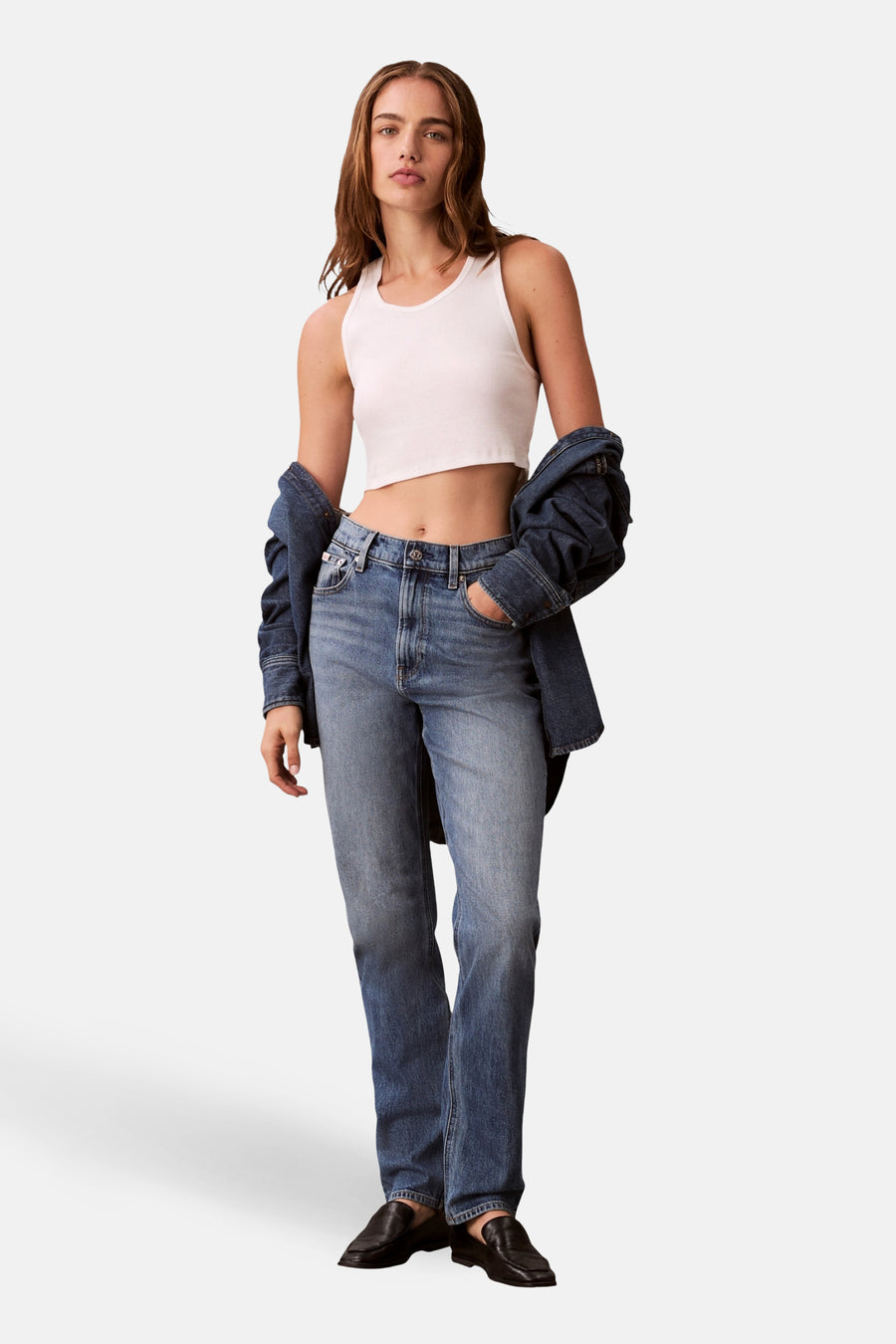 Jean mom en denim bleu moyen de Calvin Klein, porté avec un débardeur blanc et une veste en jean.
