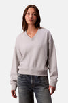 Sweat gris de Calvin Klein, avec un col en V et porté avec un jean bleu.