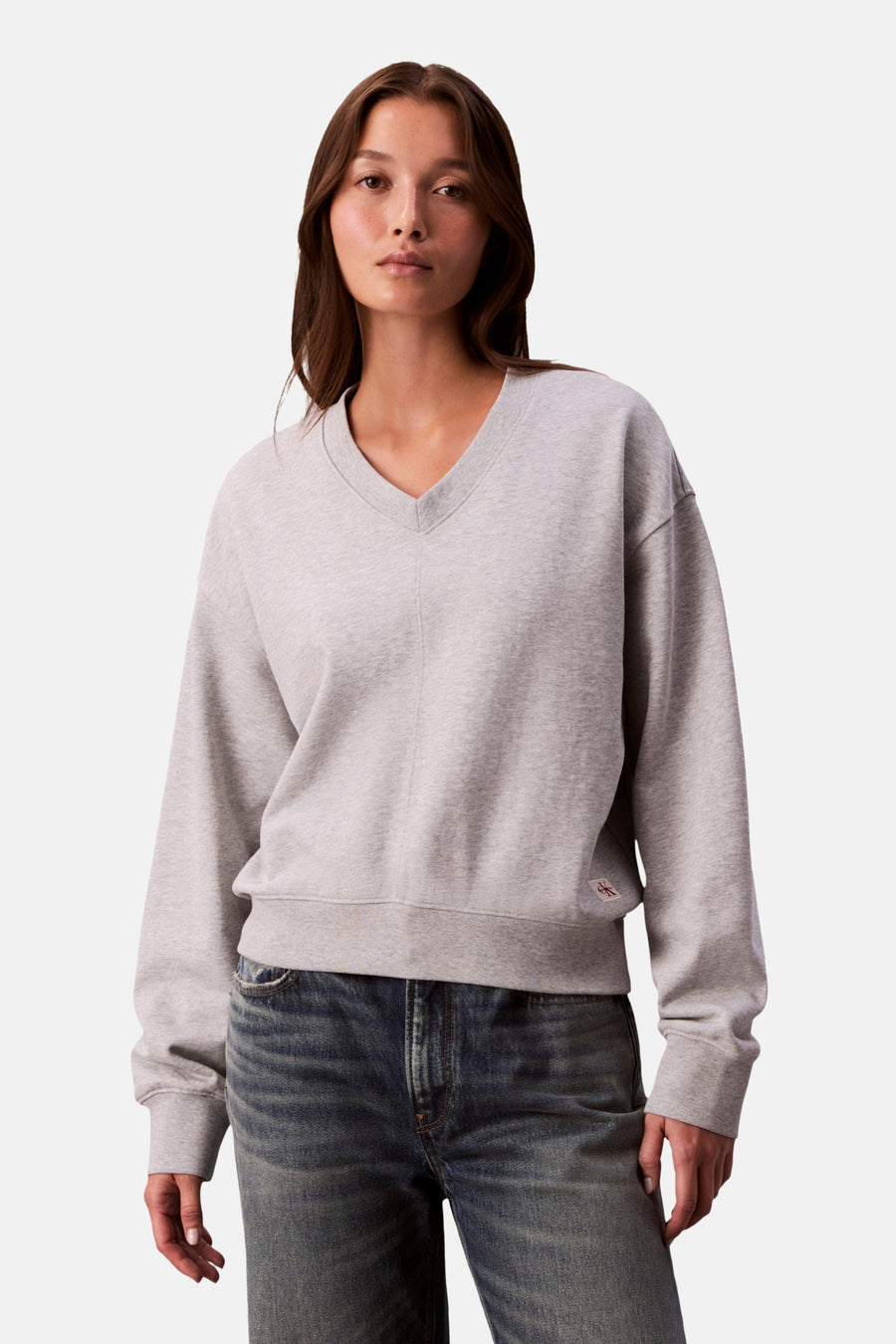 Sweat gris de Calvin Klein, avec un col en V et porté avec un jean bleu.