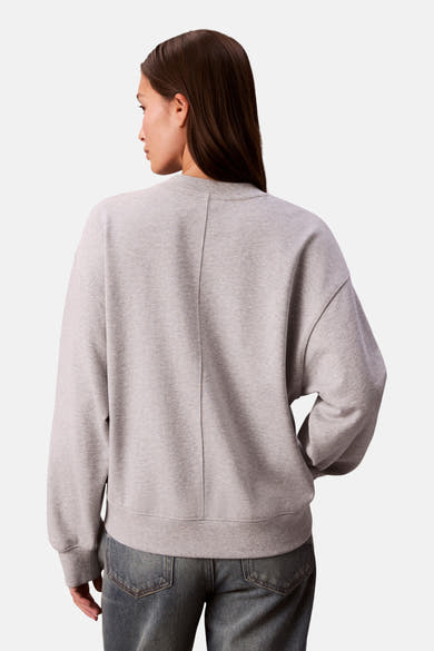 Sweat-shirt gris chiné de Calvin Klein, coupe ample avec couture verticale au dos, porté avec un jean.