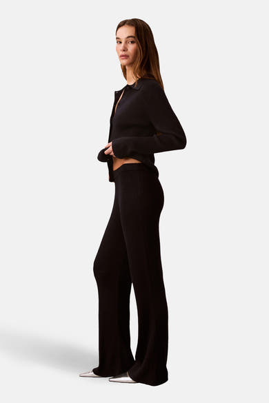 Pantalon bleu van Calvin Klein, coupe évasée et matière côtelée, porté avec un cardigan noir.
