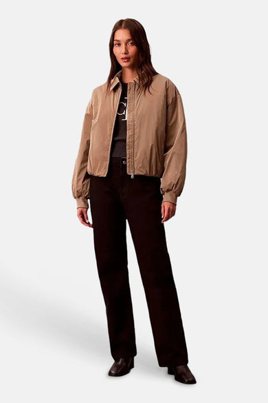 Veste courte beige de Calvin Klein, style bomber, portée sur un haut et un pantalon sombres.