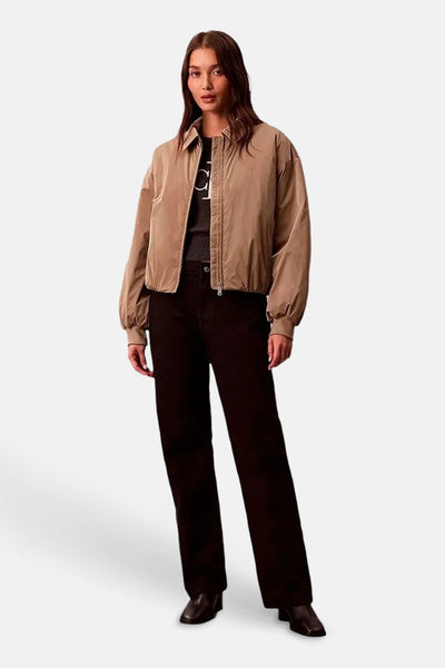 Veste courte beige de Calvin Klein, style bomber, portée sur un haut et un pantalon sombres.