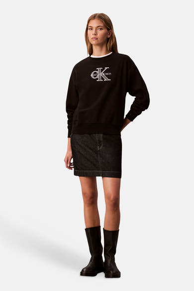 Zwart sweatshirt met ronde hals van Calvin Klein, gedragen met een korte spijkerrok en hoge zwarte laarzen.