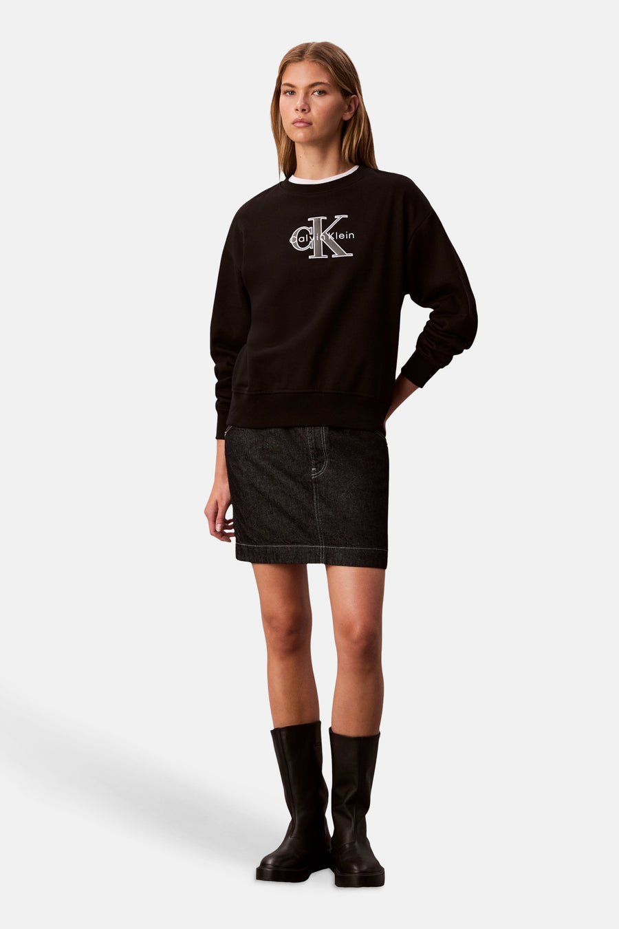 Zwart sweatshirt met ronde hals van Calvin Klein, gedragen met een korte spijkerrok en hoge zwarte laarzen.