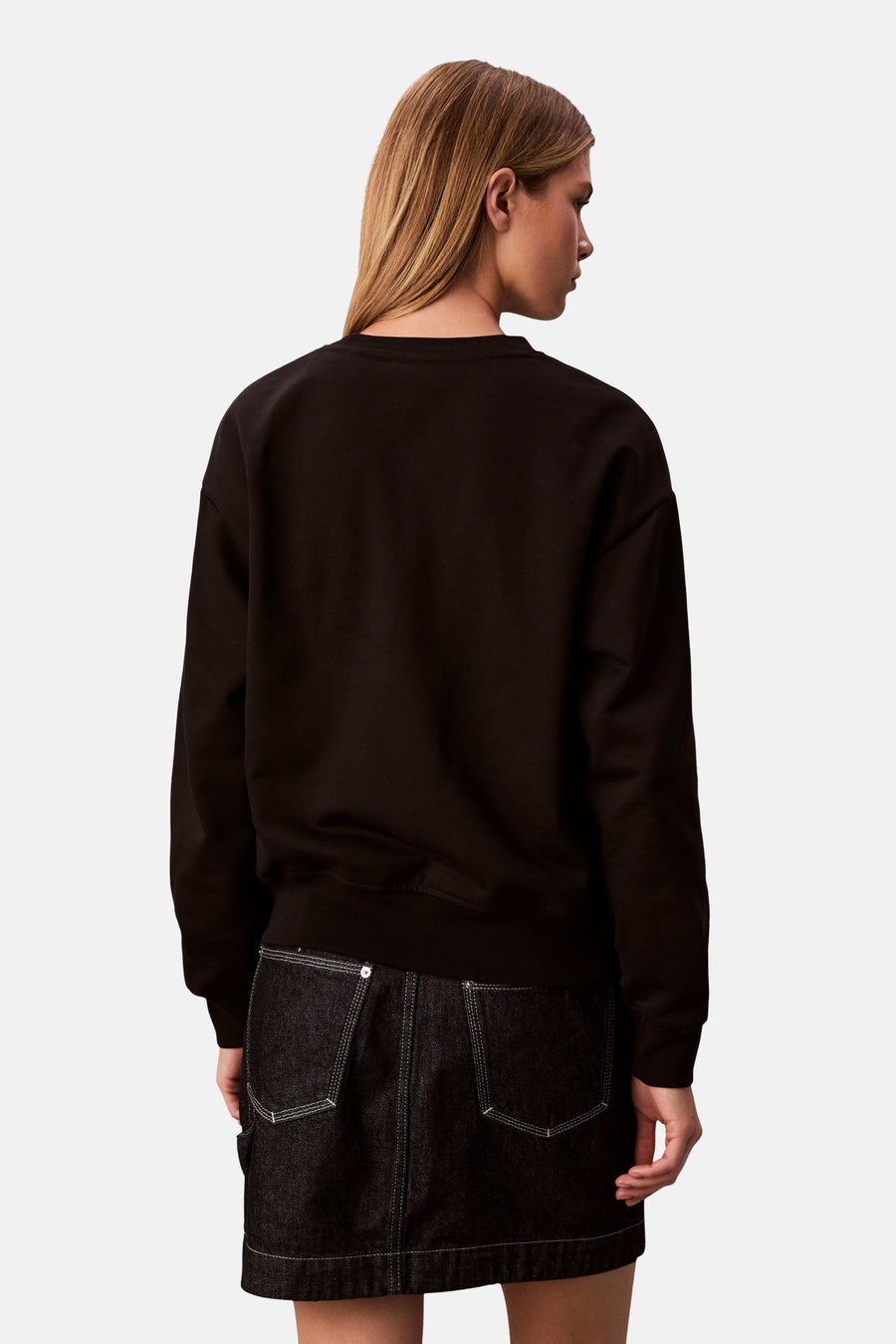 Zwart sweatshirt met ronde hals van Calvin Klein, gedragen met een korte donkerblauwe spijkerrok.
