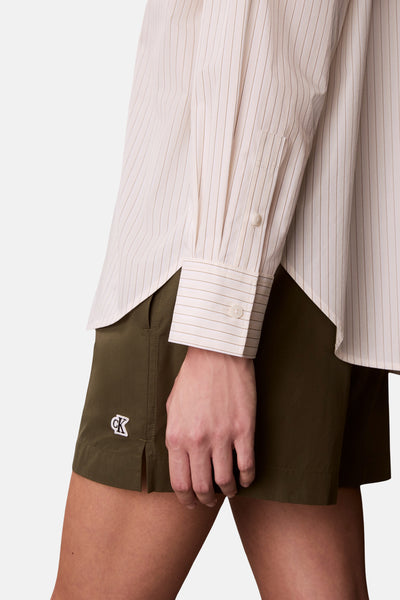 Beige gestreept overhemd met lange mouwen van Calvin Klein, met knopen op de mouw en gedragen met een kaki short.