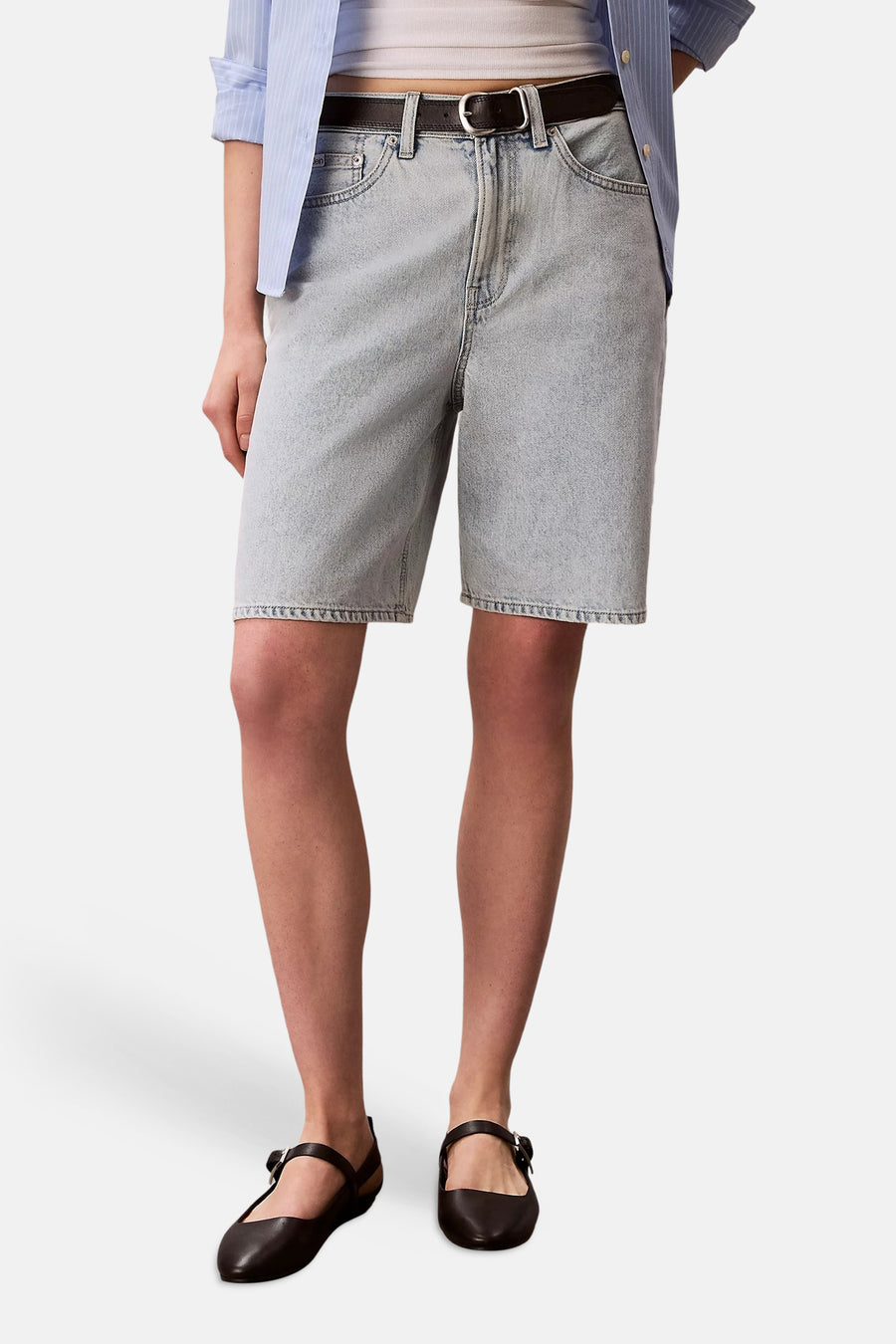 Short en denim bleu clair de Calvin Klein, porté avec une chemise rayée et des chaussures noires à bride.
