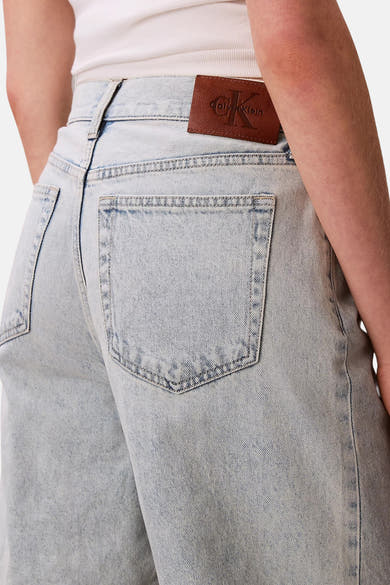 Short en denim bleu clair de Calvin Klein, avec poche arrière et étiquette en cuir marron.
