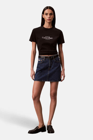 T-shirt noir à manches courtes de Calvin Klein, avec un logo blanc sur le devant, porté avec une jupe en jean.