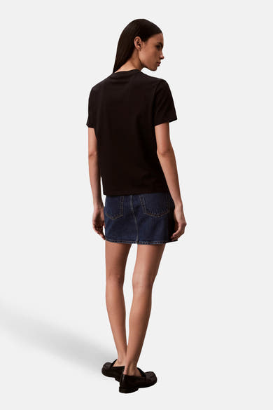 T-shirt noir de Calvin Klein, porté avec une jupe en jean bleu foncé et des chaussures noires.