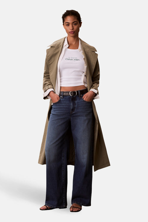 Débardeur blanc de Calvin Klein, porté sous une chemise et un trench coat beige, avec un jean ample.