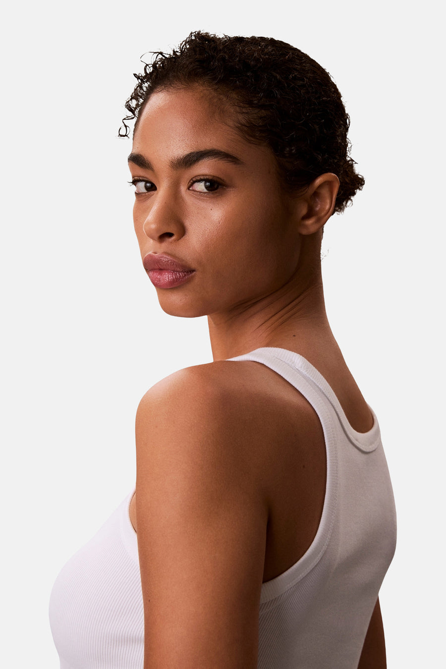 Witte tanktop van Calvin Klein, gedragen door een model dat over haar schouder kijkt.
