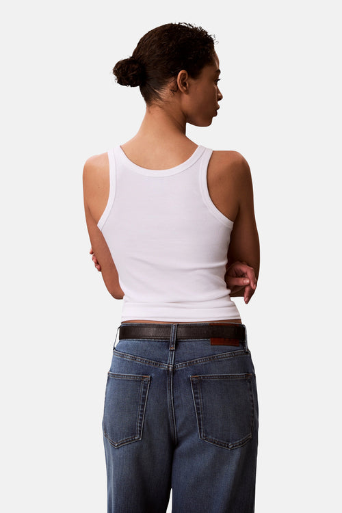 Débardeur blanc de Calvin Klein, en tricot côtelé, porté avec un jean bleu et une ceinture en cuir marron, vue de dos.